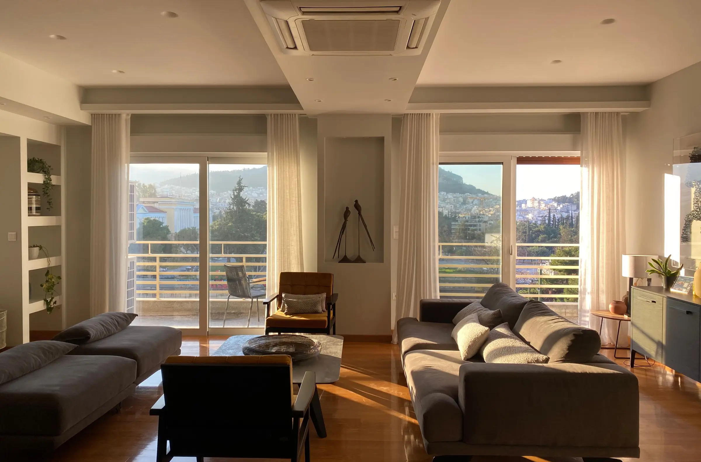 A calm living room in warm evening light, with a city view through tall windows